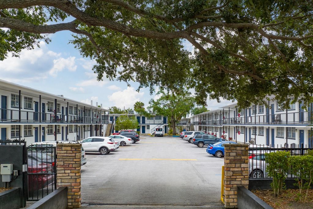 rows of apartment buildings with cars parked outside and a tree hanging overhead.