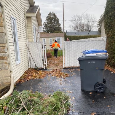 Person in orange jacket walking through a yard gate on a fall day.