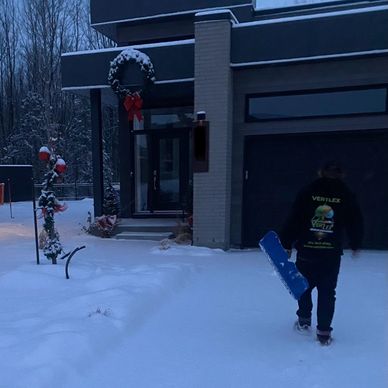 Person walking in snow toward a modern house decorated for Christmas.