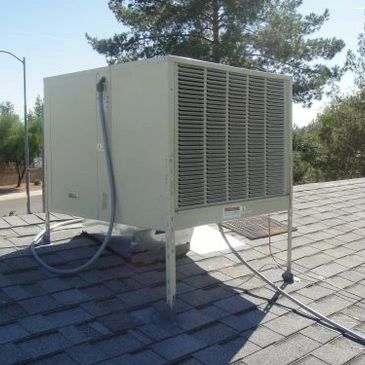 A rooftop air conditioning unit on a shingled roof under a clear sky.