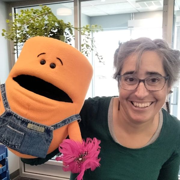 smiling woman with glasses holding a carrot puppet