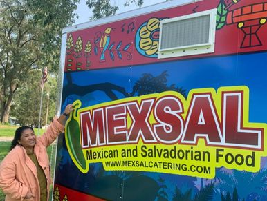 Woman standing next to a colorful food truck advertising Mexican and Salvadorian food.