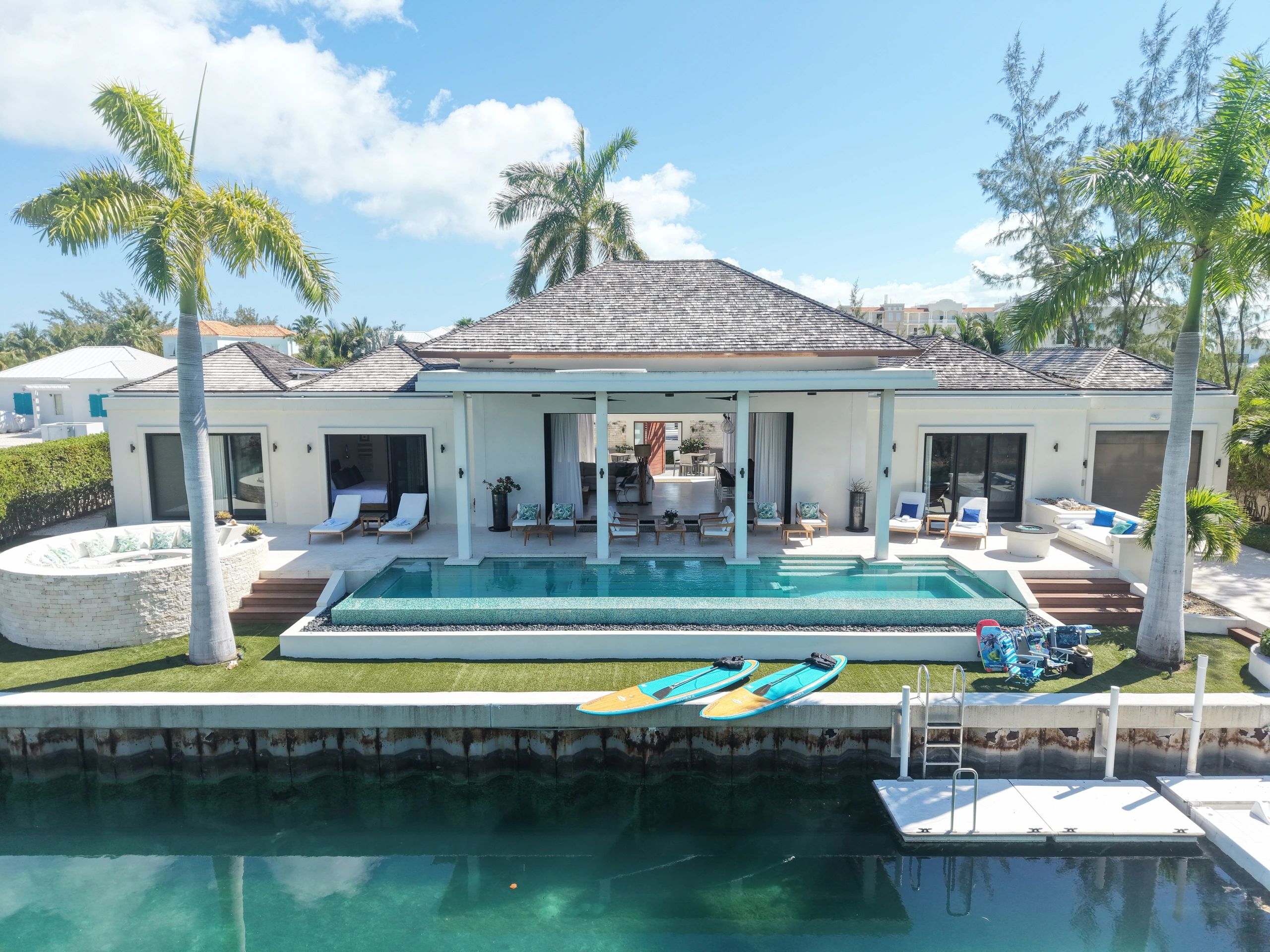 Waterside view of Casa Caoba luxury canal-front villa in Leeward, Providenciales, Turks and Caicos, showcasing the heated infinity pool, private dock, kayaks, paddleboards, and covered lanai