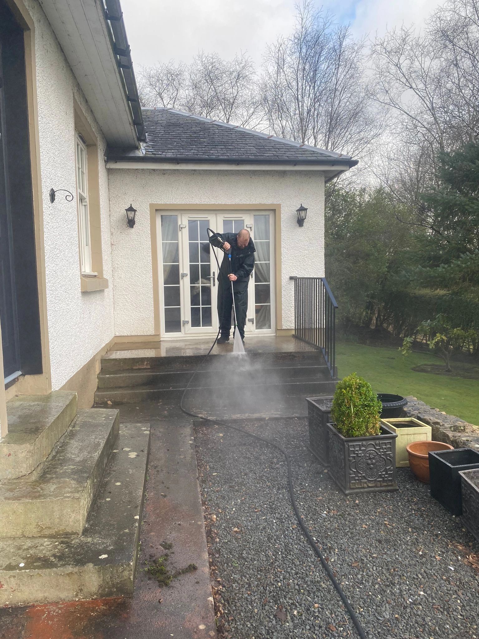 A man power washing the steps of a house on a cloudy day.