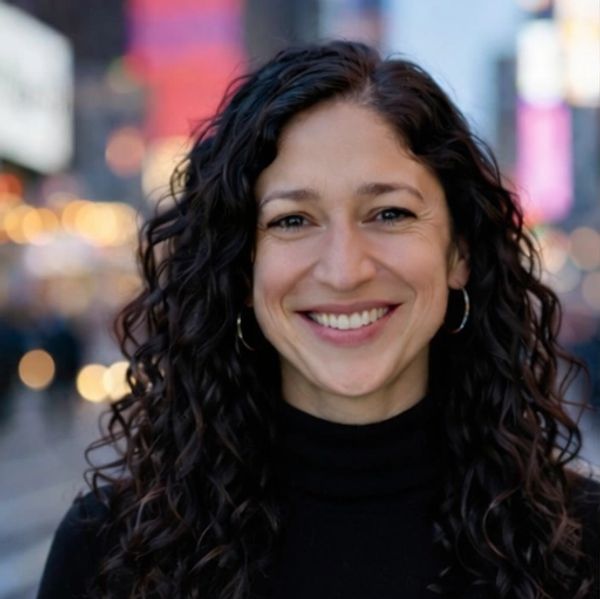 Smiling woman with curly hair in urban evening setting.