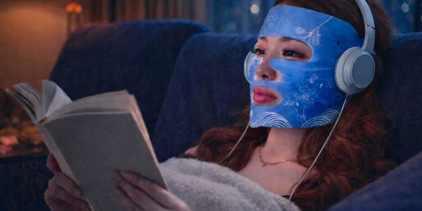 Person reading a book while wearing a blue LED face mask and headphones.