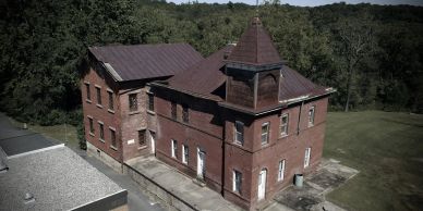 Old brick building with a tower surrounded by greenery.