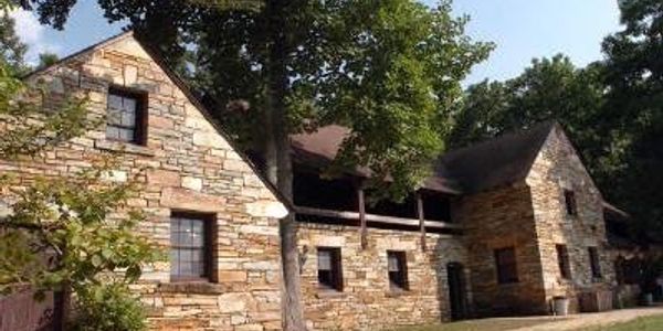 Stone house with multiple windows and trees around.