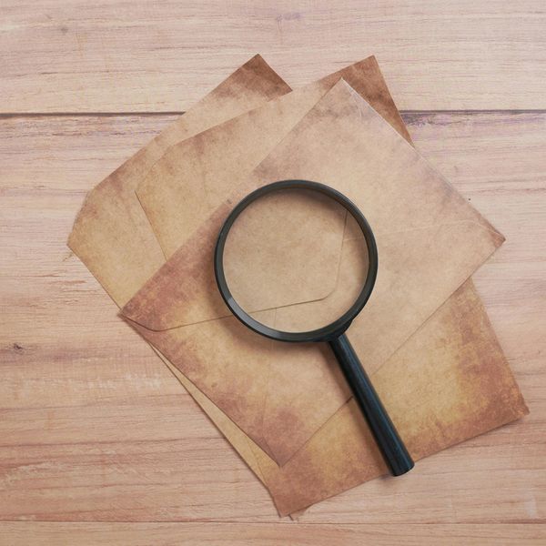 Magnifying glass on vintage envelopes on wooden surface.