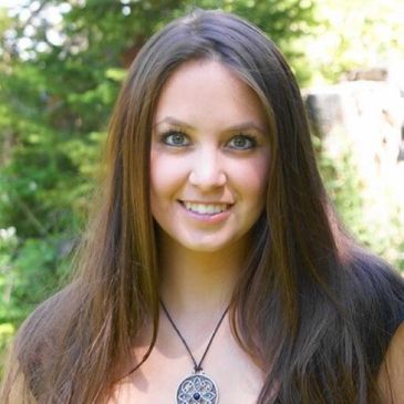 Smiling woman with long brown hair outdoors in natural light.