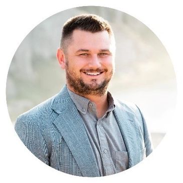 Smiling man in a grey blazer and shirt posing outdoors.