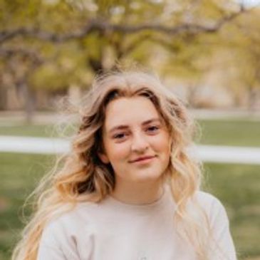 Young woman with blonde hair smiling outdoors in a park.