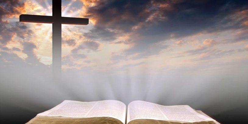 Open Bible with a glowing cross against a dramatic sky.