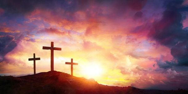 Three crosses on a hill at sunset with vibrant sky colors.