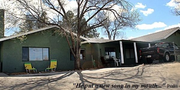 Green house with outdoor chairs and a Bible verse overlay.
