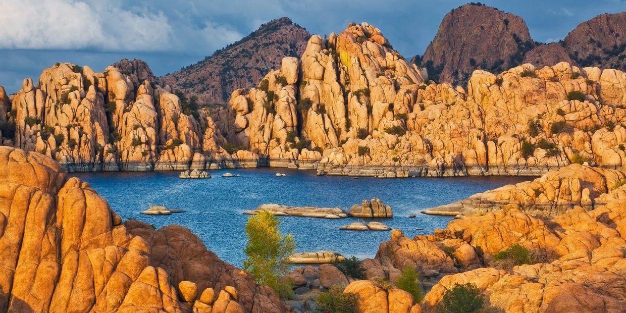 Sunlit rocky landscape surrounding a serene blue lake with distant mountains.