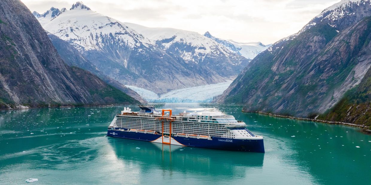 A cruise ship sailing through a fjord surrounded by snow-capped mountains.
