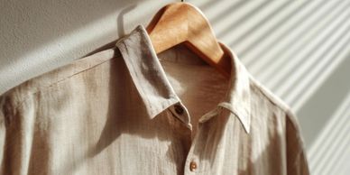 Beige shirt hanging on a wooden hanger with sunlight casting shadows.