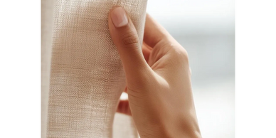 Hand gently touching a beige curtain in soft natural light.