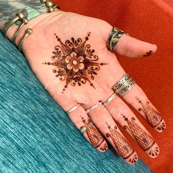 Intricate henna design on palm and fingers adorned with silver rings and bracelets.