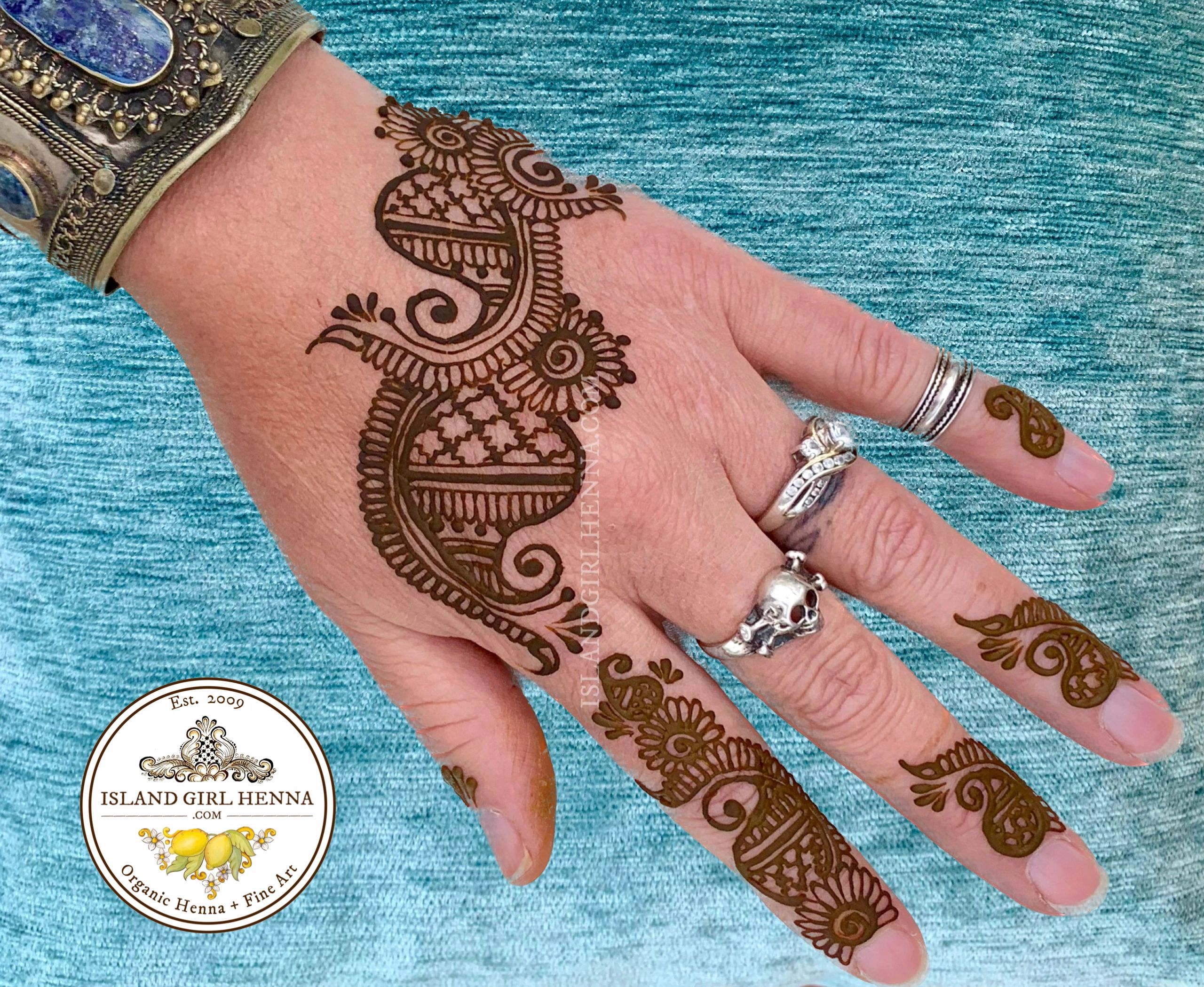 Intricate henna design on hand with rings and bracelet.