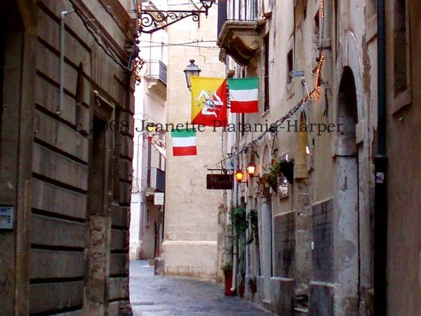 Narrow European street adorned with Italian flags and warm street lamps.