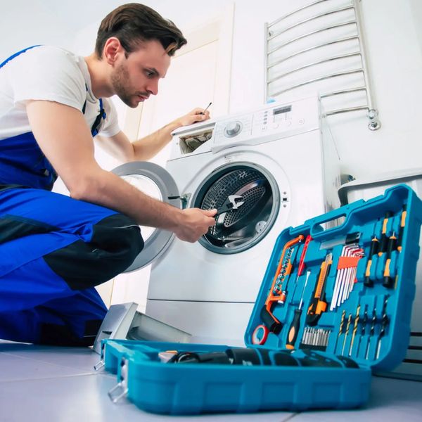 Technician repairing a front-load washing machine with tools.