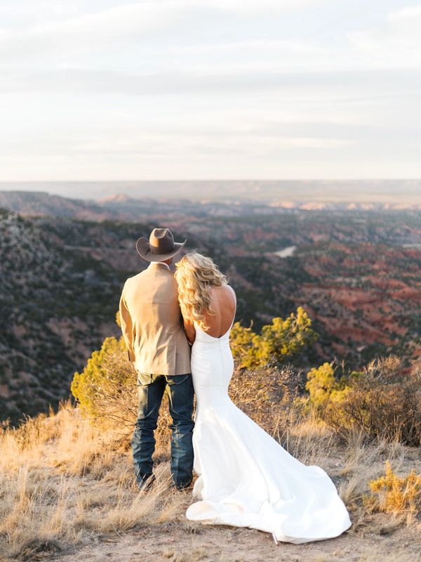 A couple in wedding attire stands overlooking a scenic canyon landscape.