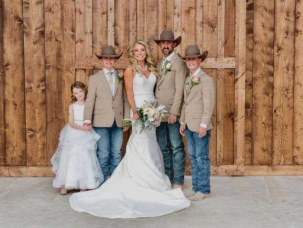 A wedding party with cowboy hats in front of a wooden backdrop.
