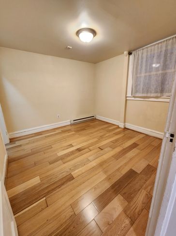 Empty room with wooden flooring and a window covered by a sheer curtain.