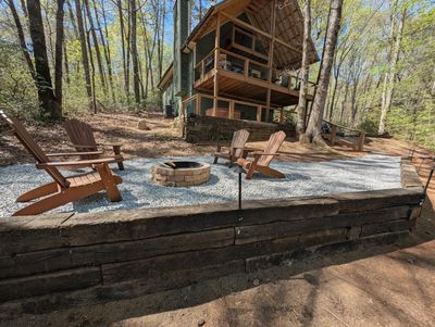 Cozy outdoor seating and fire pit by a wooden cabin in the woods.