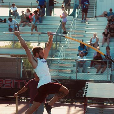 Athlete mid-jump in a pole vault event at a track meet.