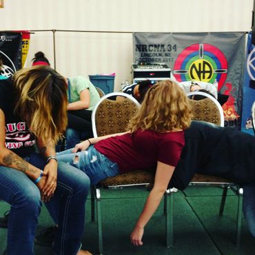 People sitting slumped over on chairs in a room with banners in the background.