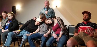 People appear hypnotized on stage with a man holding a microphone behind them.