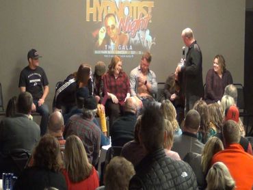 Hypnotist entertaining a crowd with volunteers on stage at a comedy night event.