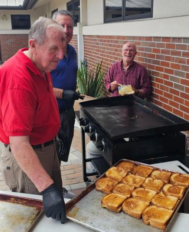 Three men grilling toasted bread outdoors.