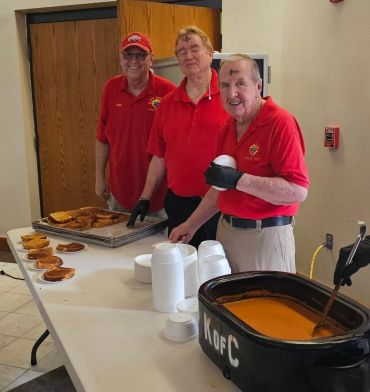 Three men serving food and soup in a community setting.