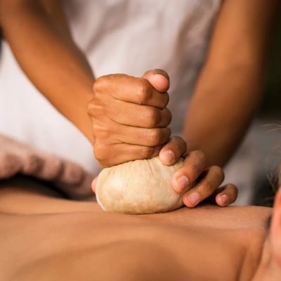 Therapist applying herbal compress massage on a person's back.