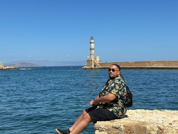 Man sitting by the sea with a lighthouse in the background.