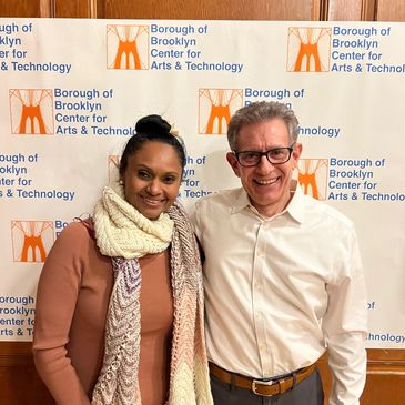 Two people smiling in front of a Borough of Brooklyn Center for Arts &amp; Technology banner.