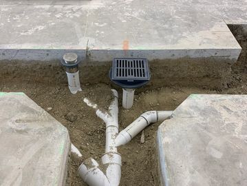 Exposed underground plumbing pipes and a floor drain in a construction site.