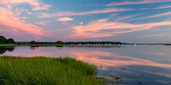 Sunset over a calm lake with green grass in the foreground.