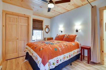 Bedroom with warm orange floral quilt, wooden ceiling beams, and a plain white door.