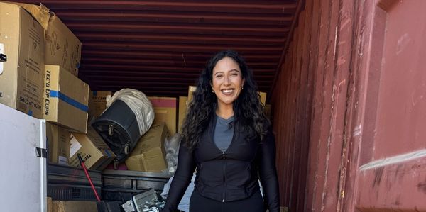 Smiling woman standing inside a container filled with boxes.