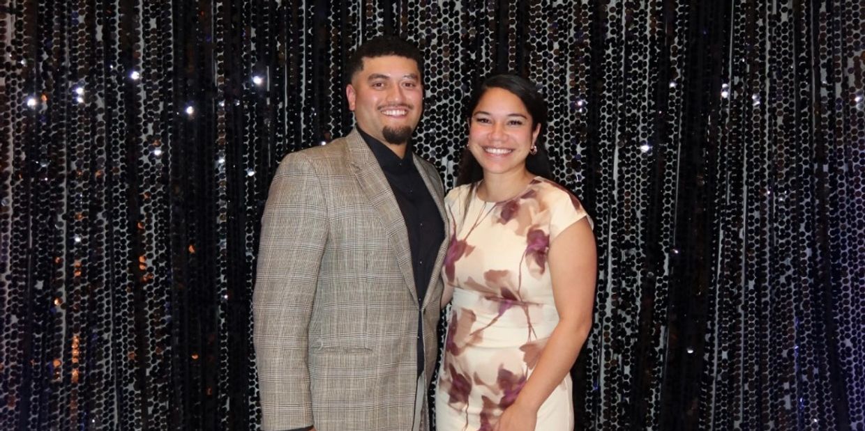 A smiling couple posing in front of a black sequin backdrop, dressed formally.