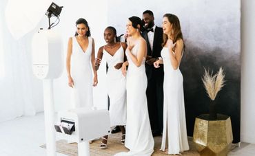 A group of elegantly dressed people in white gowns and a tuxedo posing for a photo.