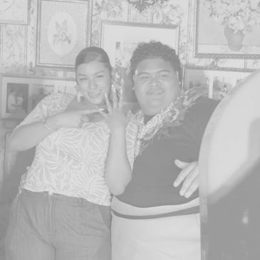 Two people smiling and showing a ring in a room with floral wallpaper and framed pictures.