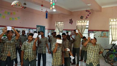 Group of men in matching shirts holding up drawings in a decorated room.
