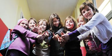 Group of children smiling and showing thumbs up together indoors.