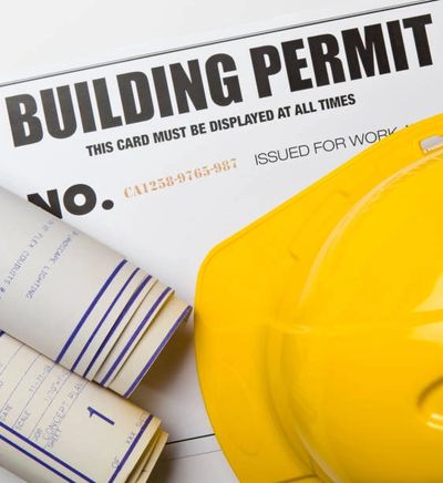 Building permit card with blueprints and yellow hard hat.